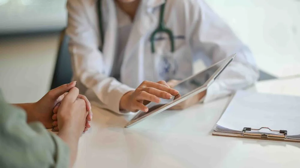 Vital Plus Pflegedienst - Aufnahme eines Arztes, der einem Patienten einige Informationen auf einem digitalen Tablet zeigt