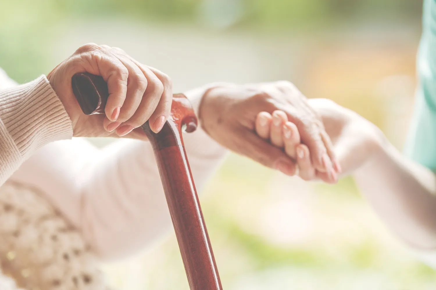 Vital Plus Pflegedienst - Nahaufnahme einer älteren Dame, die in der einen Hand einen Gehstock und in der anderen die Hand einer Krankenschwester hält