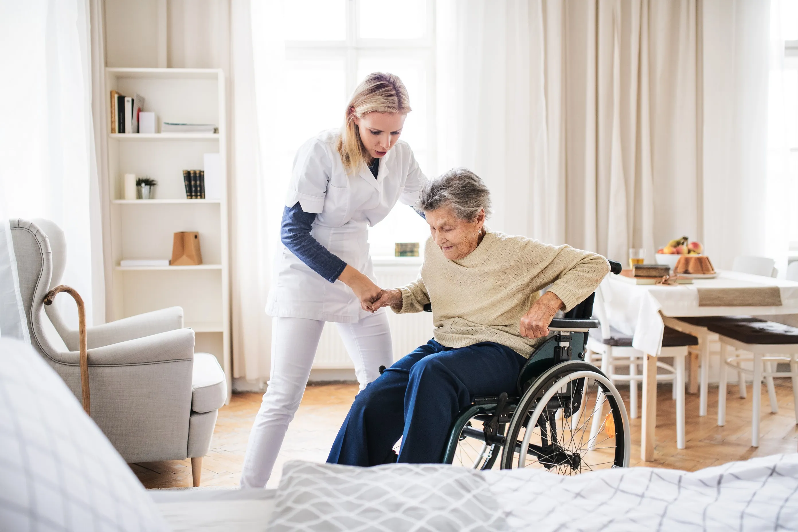 Vital Plus Pflegedienst - Eine Gesundheitsberaterin hilft einer älteren Frau beim Aufstehen aus dem Rollstuhl