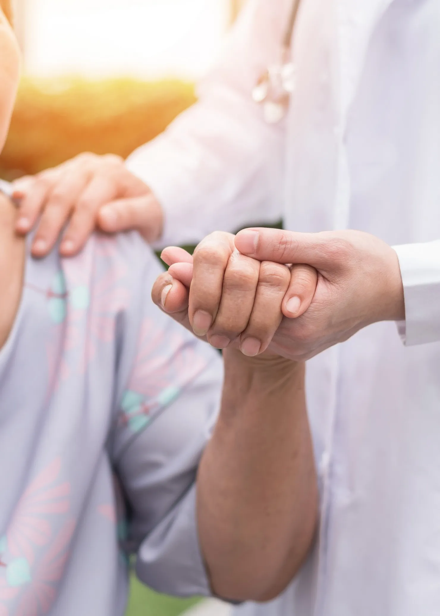 Vital Plus Pflegedienst - Älterer demenzkranker Patient in einem Hospiz, der die Hand eines geriatrischen Arztes hält und sich über die medizinische Versorgung durch eine Pflegerin freut